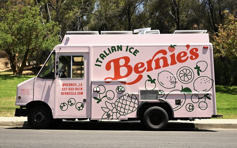 The pink Bernie&rsquo;s Italian Ice food truck parked curbside, covered in green fruit line art