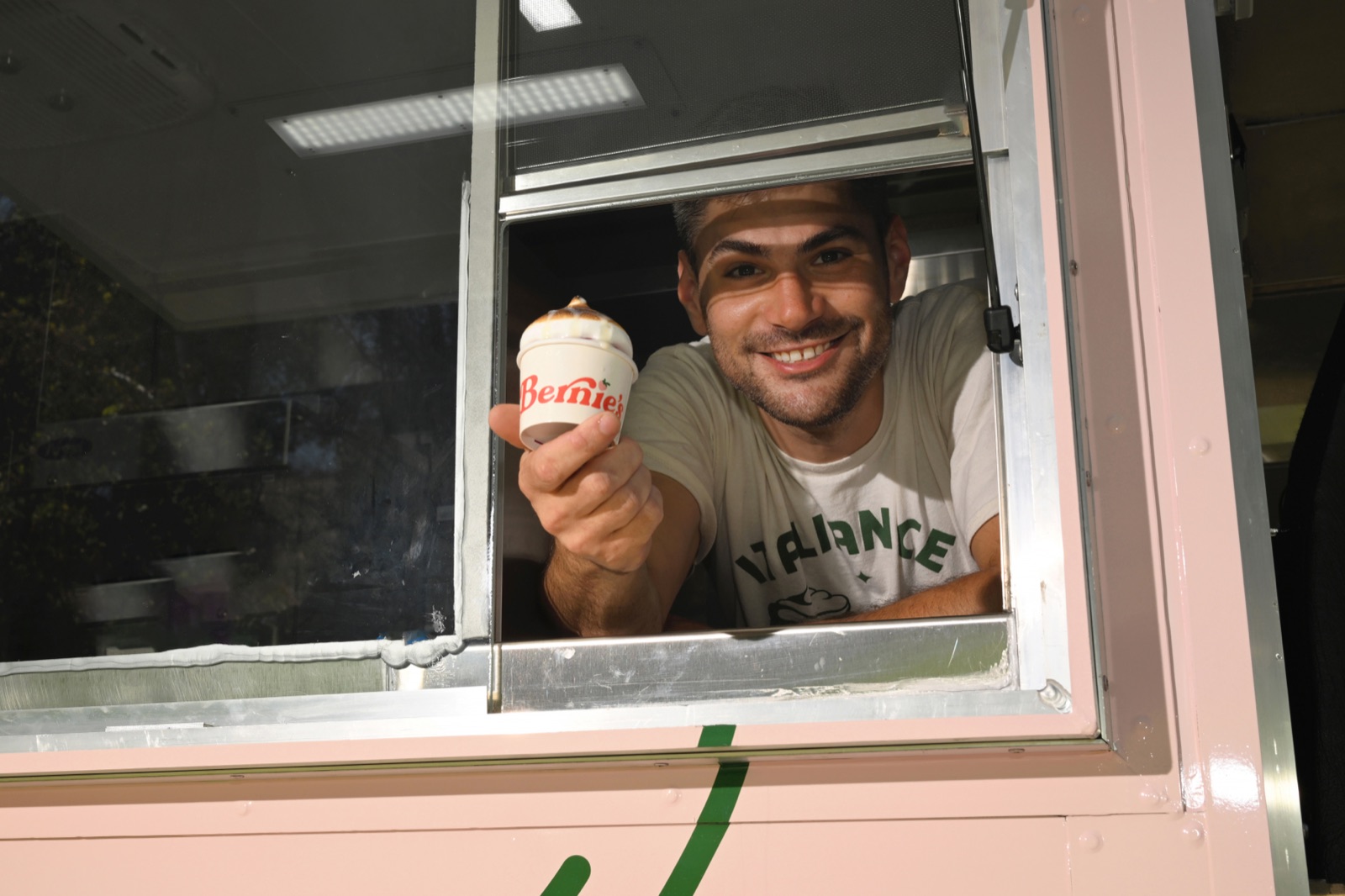 A smiling Bernie&rsquo;s team member at the truck&rsquo;s serving window, handing out a cup of Italian ice topped with torched meringue